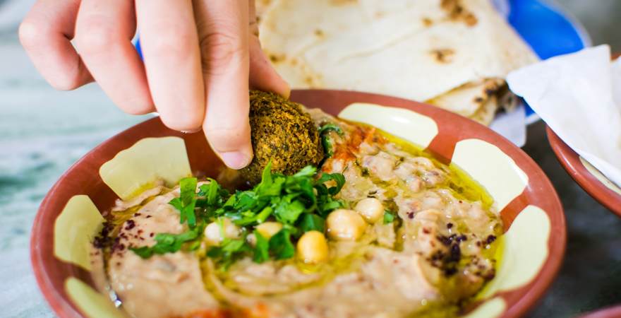 Eine Hand taucht Falafel in Hummus, ein typisches Gericht in Israel