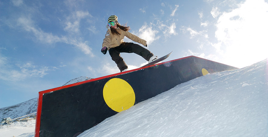 Frau auf einem Snowboard über einem Hinderniss