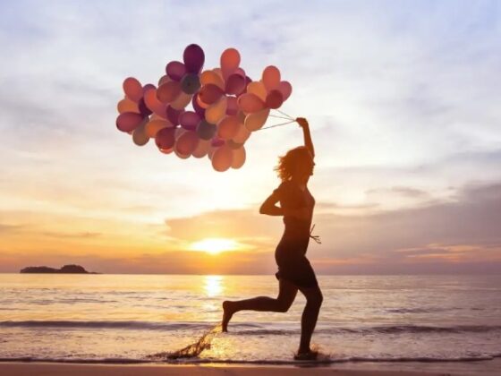 Glückliche Frau am Strand zum Sonnenuntergang mit Luftballons