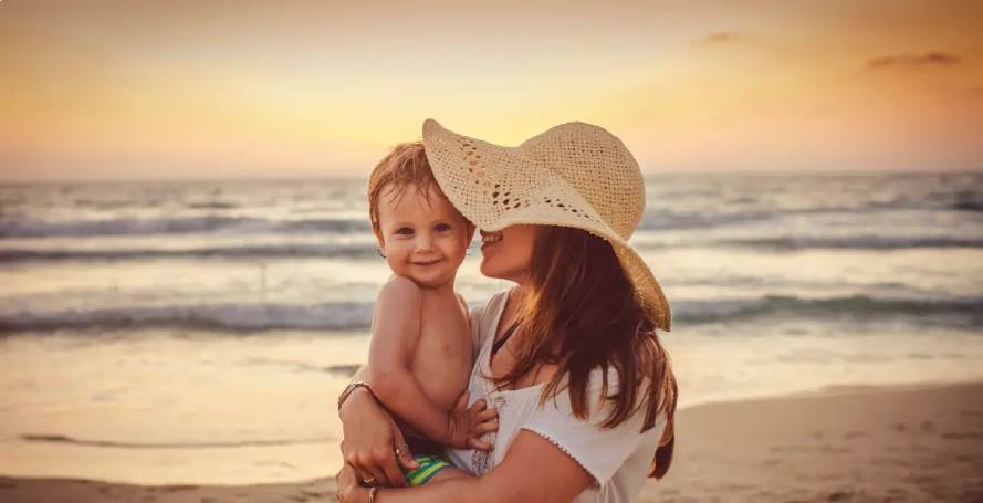 Mutter mit Kind auf dem Arm am Strand bei Sonnenuntergang