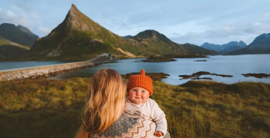 Frau mit Baby in roter Mütze vor See und Bergen